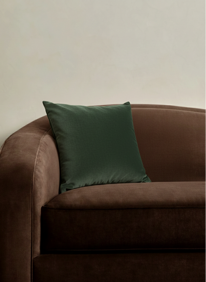 Brown sofa with a green pillow against a plain wall
